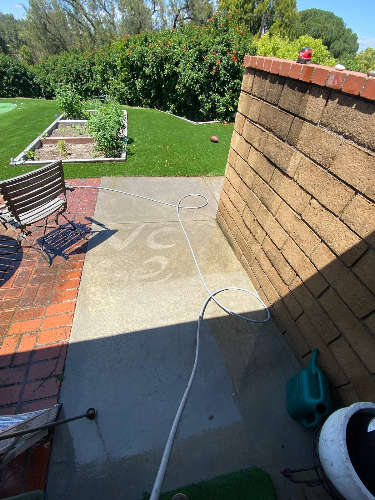 Backyard concrete patio partway through pressure washing, with the letters VC washed into the dirty concrete showing the clean versus dirty contrast